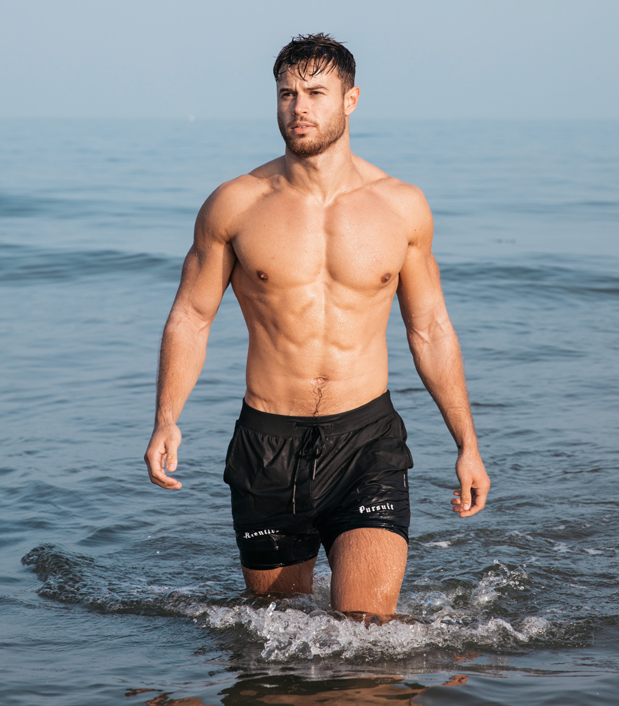 Coach steps out of the water, shirtless and posing confidently.